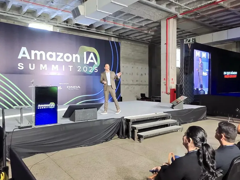 Palestrante no palco do Amazon IA Summit 2025 com o painel do evento ao fundo