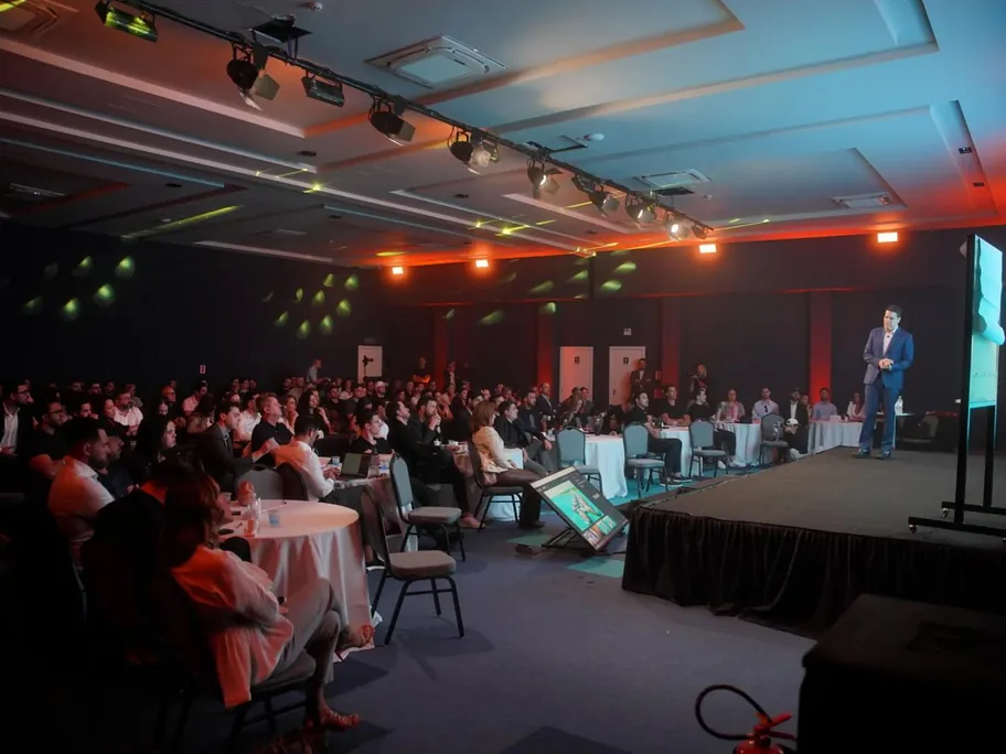 Palestrante no palco do Evento BRQ diante de um auditório lotado com iluminação colorida